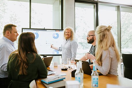 Fünf Personen besprechen sich rund um einen Bildschirm mit Grafiken.